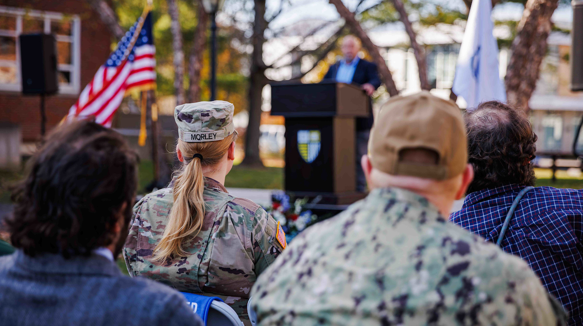 Photo of two veterans in fatigues listening to a speaker at Merrimack's Veteran's Day celebration.