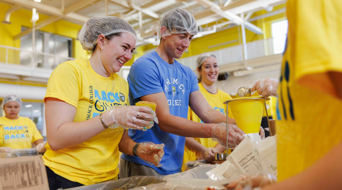 Two Merrimack students packaging nonperishable meals while smiling.