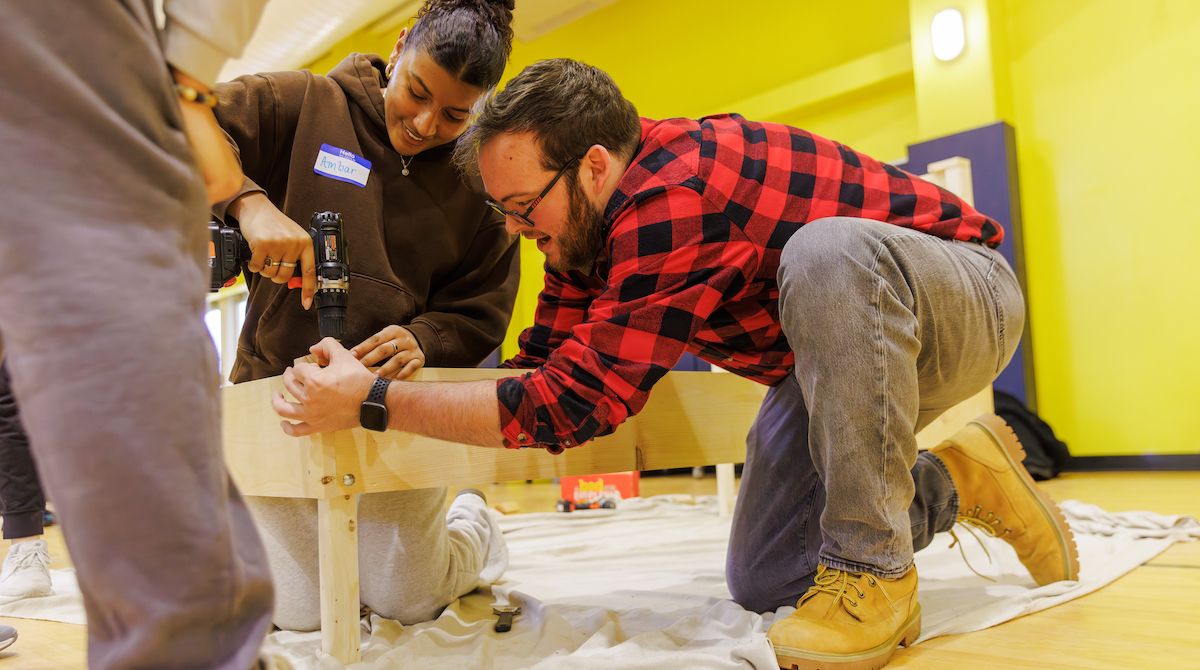 Two Merrimack College students drilling two pieces of wood together.