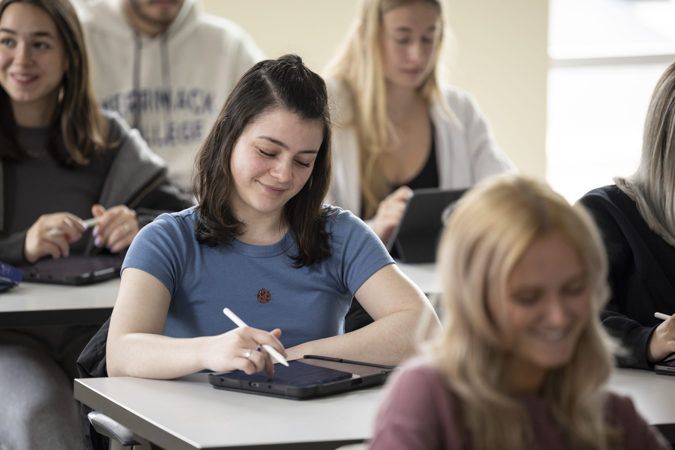 Student looking down and writing on an ipad in a classroom