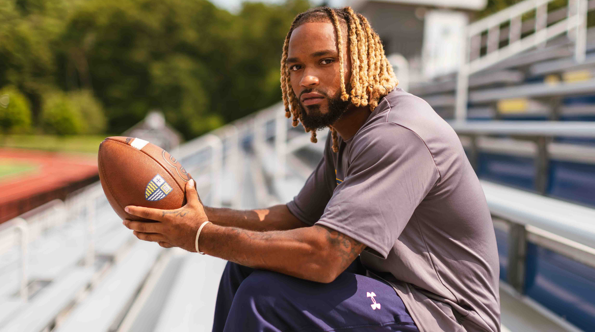 Photo of Donovan Wadley ’26 sitting on bleachers holding a football.