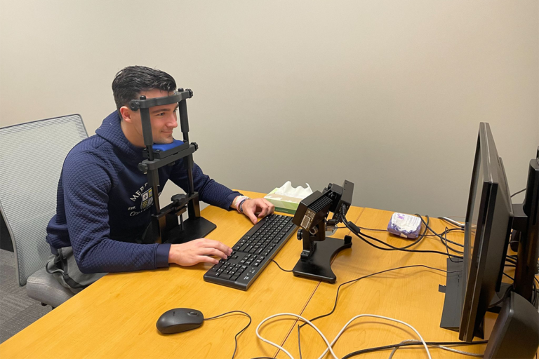 Student participating in a scan lab test with a sensor device strapped to his head while sitting at the computer.